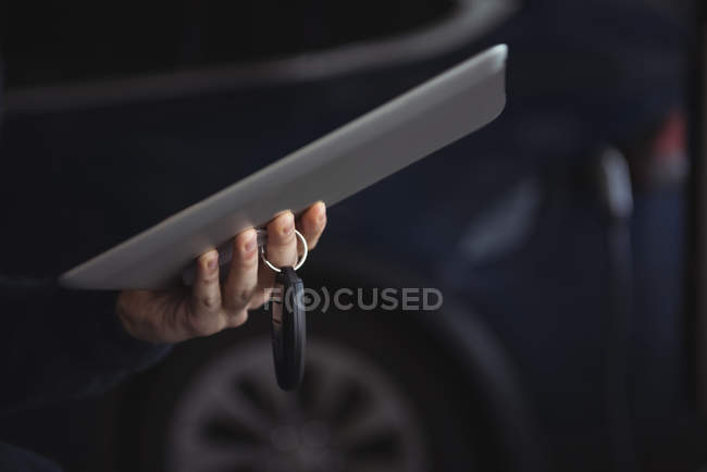 Mann hält Autoschlüssel und digitales Tablet in Garage, Nahaufnahme — Stockfoto
