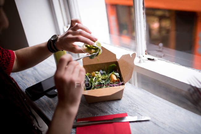 Mujer vertiendo salsa verde en una ensalada en la cafetería - foto de stock