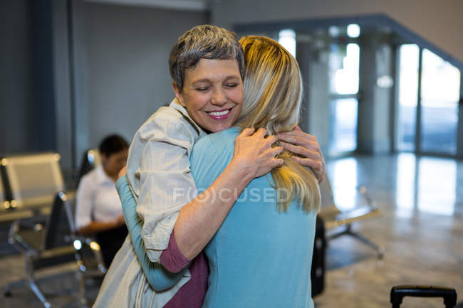 Amigos abrazándose en la sala de espera en la terminal del aeropuerto - foto de stock