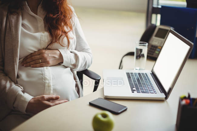 Mid section of pregnant businesswoman holding belly in office — Stock Photo