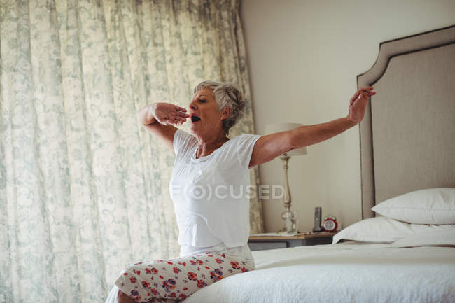 Seniorin gähnt im heimischen Schlafzimmer auf Bett — Stockfoto