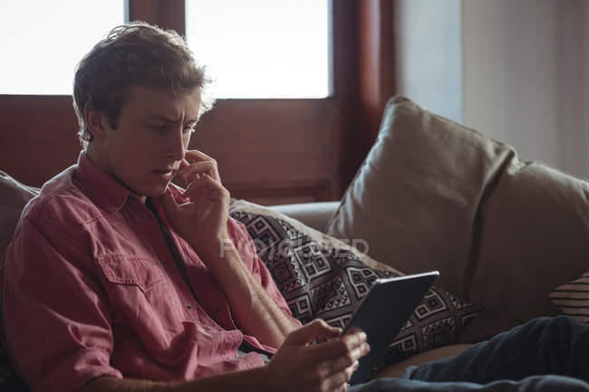 Homem sentado no sofá usando um tablet digital na sala de estar — Fotografia de Stock