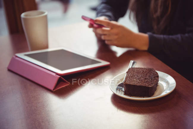 Woman using mobile phone in restaurant, dessert and digital tablet on table — Stock Photo