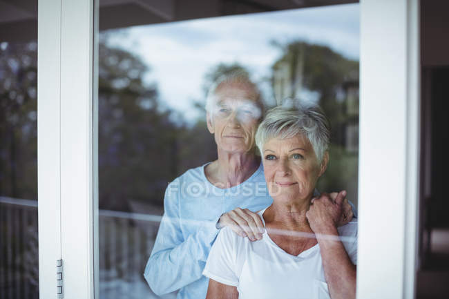 Старшая пара смотрит в окно дома — стоковое фото