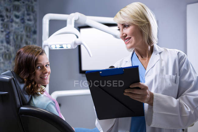 Dentista sorridente con appunti e paziente presso la clinica dentistica — Foto stock