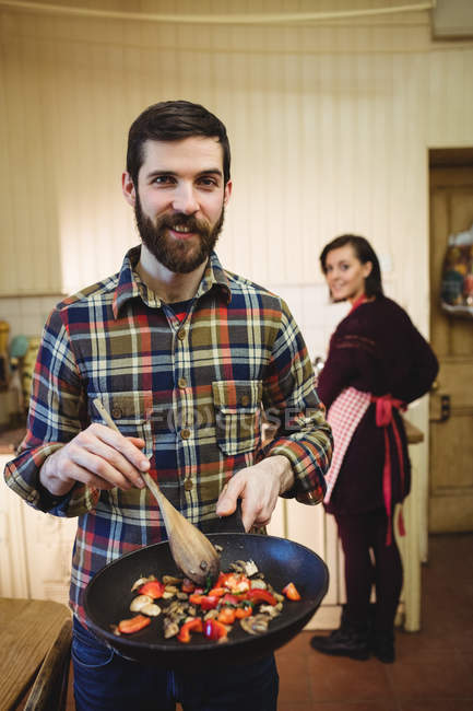 Man preparing food in kitchen at home with woman in background — Stock Photo