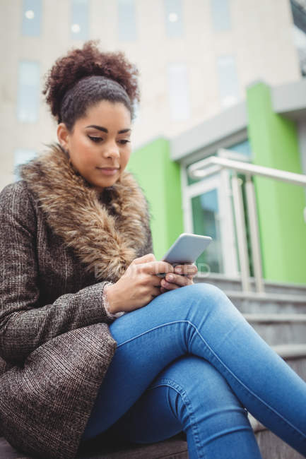 Niedrigwinkel-Ansicht einer Frau, die ihr Handy benutzt, während sie auf Stufen sitzt — Stockfoto