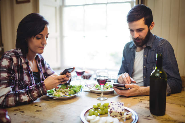 Pareja usando el teléfono móvil mientras cenan en casa - foto de stock
