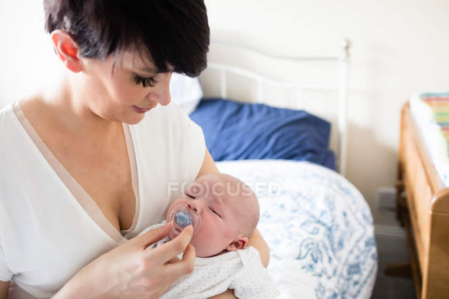 Мама кладет манекен в рот ребенку дома — стоковое фото
