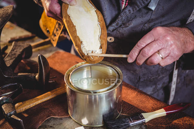 Primer plano del zapatero aplicando pegamento en la suela del zapato en el taller - foto de stock