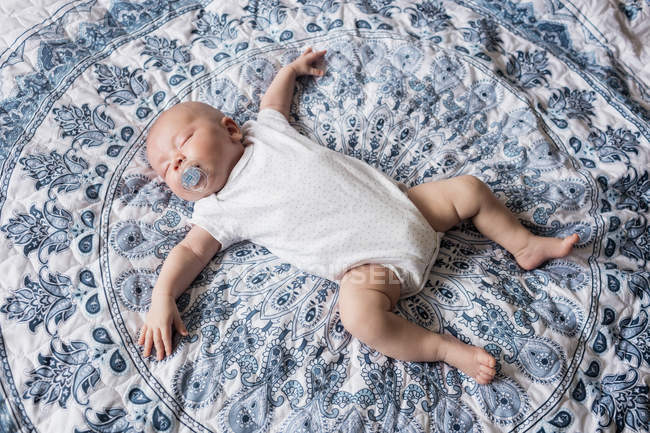 Bebé durmiendo con maniquí en la boca en la cama en casa - foto de stock