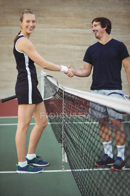Jugadores sonrientes de tenis estrechando la mano en la cancha antes del partido - foto de stock