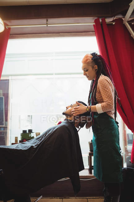 Hombre recibiendo masaje facial de peluquero femenino en peluquería - foto de stock