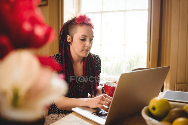 Mujer joven usando el ordenador portátil mientras está sentado en casa - foto de stock