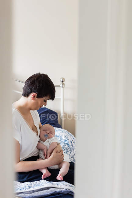 Baby with dummy sleeping on mother arm on bed in bedroom — Stock Photo
