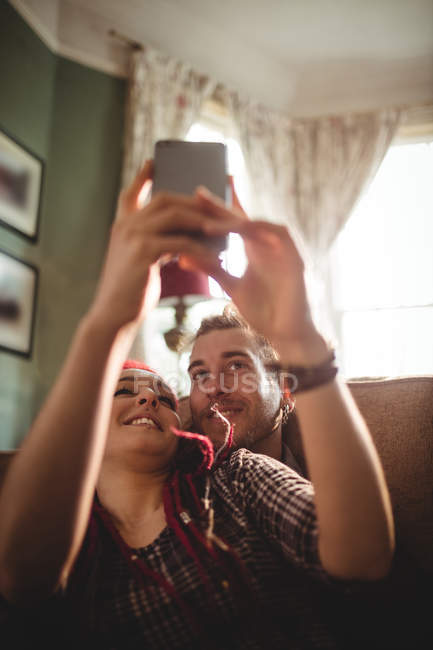Casal feliz tomando selfie enquanto relaxa no sofá em casa — Fotografia de Stock