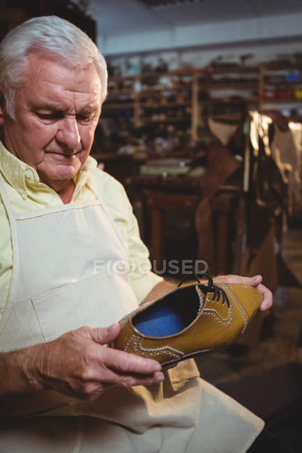 Sapateiro pensativo examinando um sapato na oficina — Fotografia de Stock