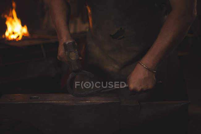Metà sezione del fabbro che tiene ferro di cavallo in metallo con pinze su incudine utilizzando martello per modellare — Foto stock