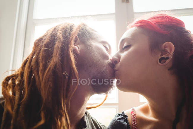 Jovem hipster casal beijos contra janela em casa — Fotografia de Stock