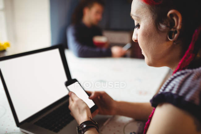 Хипстер женщина с помощью мобильного телефона и ноутбука в то время как мужчина в фоновом режиме дома — стоковое фото