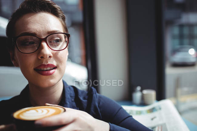 Mujer joven con taza de café mirando hacia otro lado en la cafetería - foto de stock