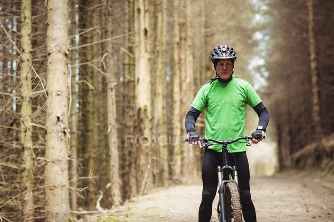 Retrato del ciclista masculino de pie junto a los árboles en el bosque - foto de stock