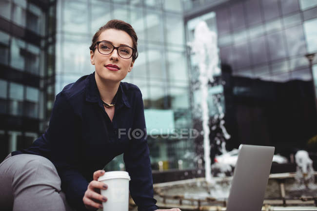 Businesswoman sitting by fountain outside office building — Stock Photo