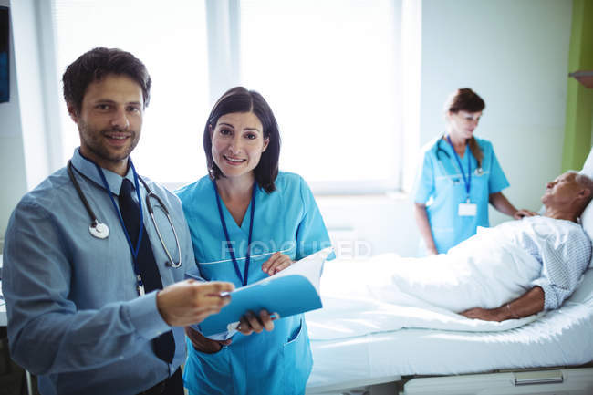 Médico y enfermera varones que interactúan sobre un informe en el hospital - foto de stock