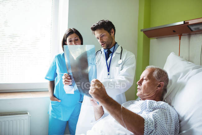 Médico e enfermeiro interagindo sobre o relatório de raios-X com o paciente no hospital — Fotografia de Stock