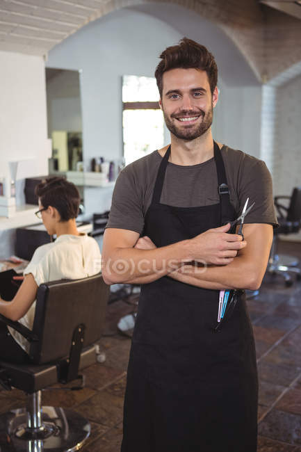 Retrato de cabeleireiro masculino de pé com os braços cruzados em um salão — Fotografia de Stock