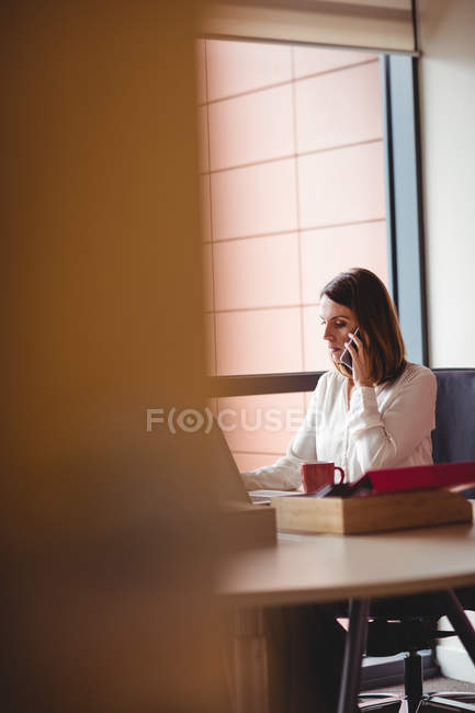 Donna d'affari che utilizza il computer portatile e parla al telefono cellulare in ufficio — Foto stock