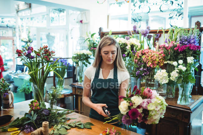 Fêmea florista aparando hastes de flores em sua loja de flores — Fotografia de Stock