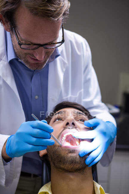 Дантист осматривает пациента с зеркалом под углом в стоматологической клинике — стоковое фото