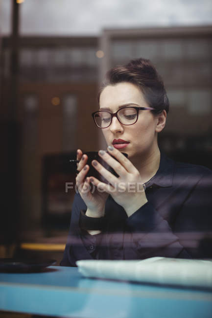 Молода жінка п'є каву в кафе, яку видно через скло — стокове фото