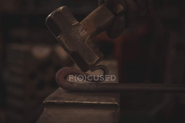 Mano de herrero trabajando en una varilla de hierro calentada en taller - foto de stock