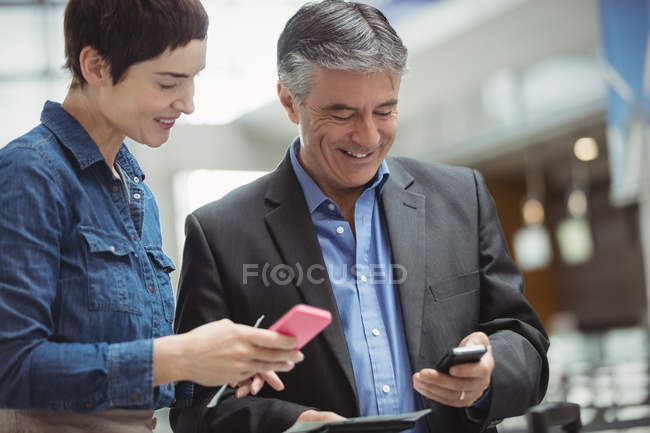 Empresários titulares de cartão de embarque e que utilizam telemóveis no terminal aeroportuário — Fotografia de Stock