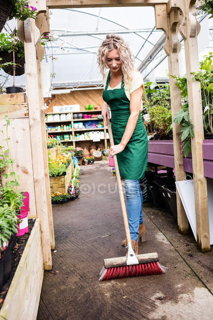 Florista varrendo chão com escova de chão no centro do jardim — Fotografia de Stock