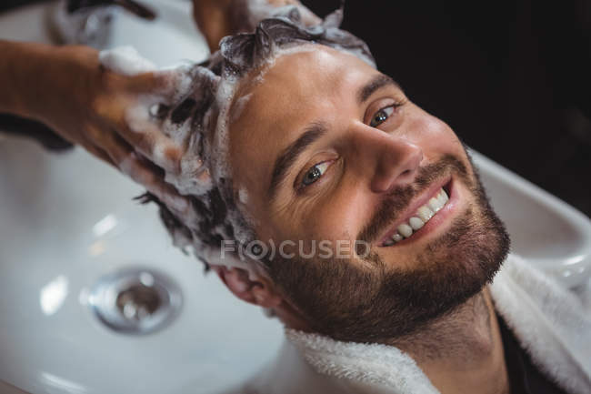 Retrato del hombre sonriente lavándose el pelo en el salón - foto de stock