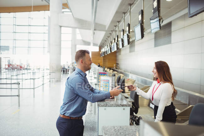Asistente de facturación de la aerolínea entrega de pasaporte al pasajero en el mostrador de facturación del aeropuerto — Stock Photo
