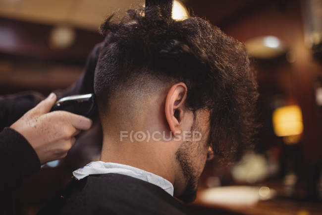 Vista trasera del hombre conseguir su pelo recortado con trimmer en la peluquería - foto de stock