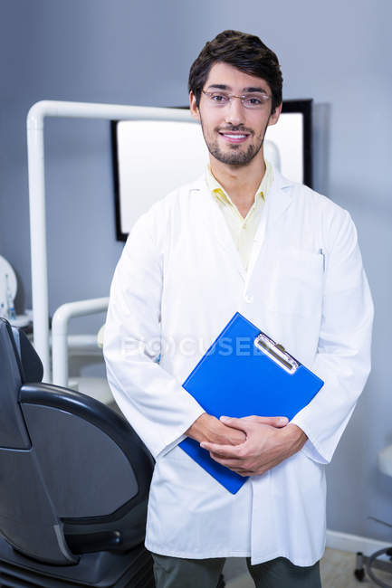 Retrato del dentista sonriente de pie con un portapapeles en la clínica dental - foto de stock
