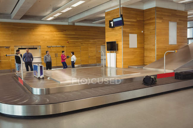 Personas que esperan equipaje en el área de reclamo de equipaje en el aeropuerto - foto de stock