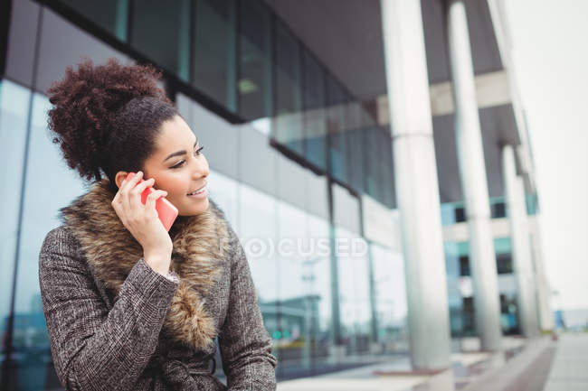 Sorrindo mulher falando ao telefone enquanto sentado contra o edifício — Fotografia de Stock