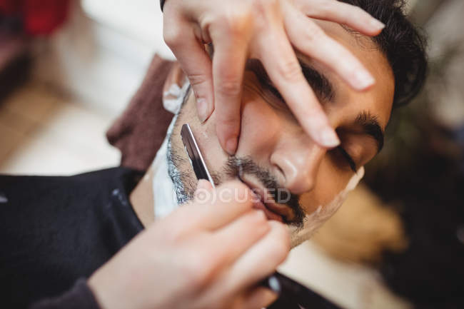 Hombre afeitándose la barba con navaja en la peluquería - foto de stock