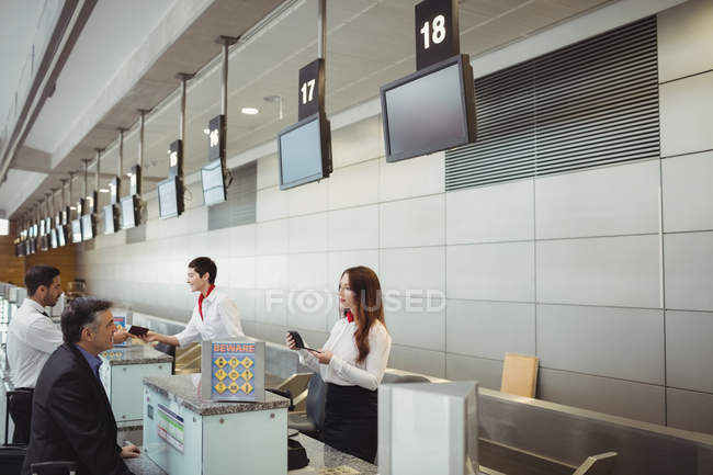Assistentes de check-in das companhias aéreas que entregam passaporte aos passageiros no balcão de check-in do aeroporto — Fotografia de Stock