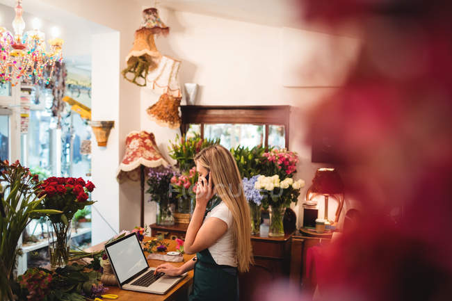 Floristin benutzt Laptop beim Telefonieren im Blumenladen — Stockfoto