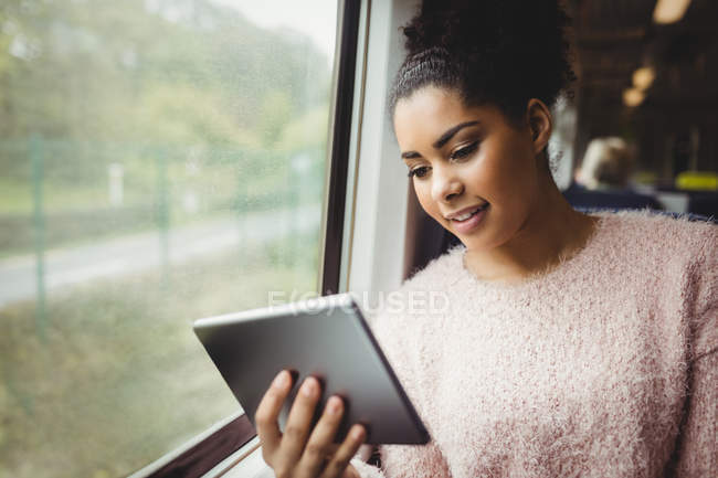 Mulher sorridente usando tablet digital enquanto está sentada no trem — Fotografia de Stock