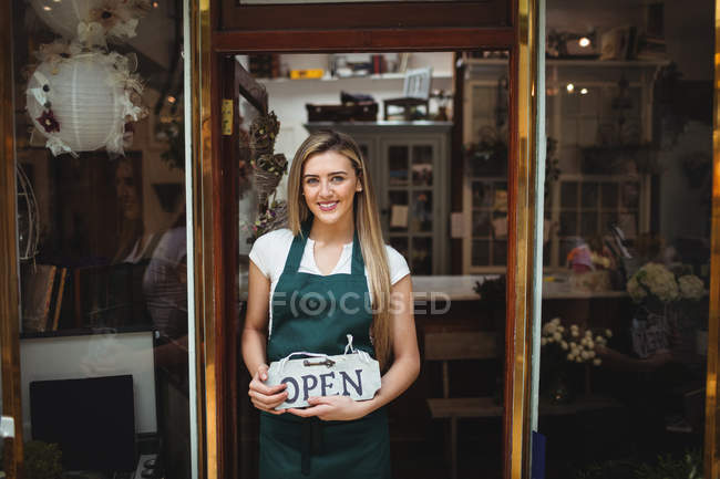 Portrait of female florist holding open signboard at her flower shop — Stock Photo