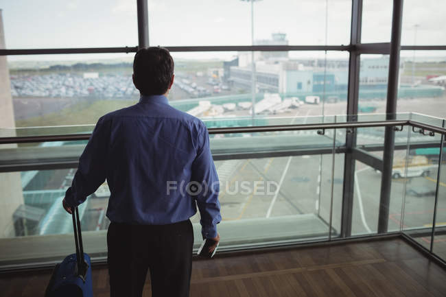 Rear view of businessman with luggage looking through glass window at airport — Stock Photo