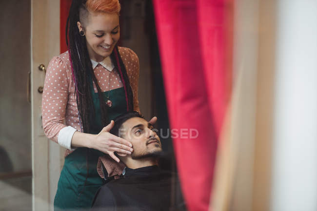 Homem recebendo massagem facial de barbeiro feminino na barbearia — Fotografia de Stock